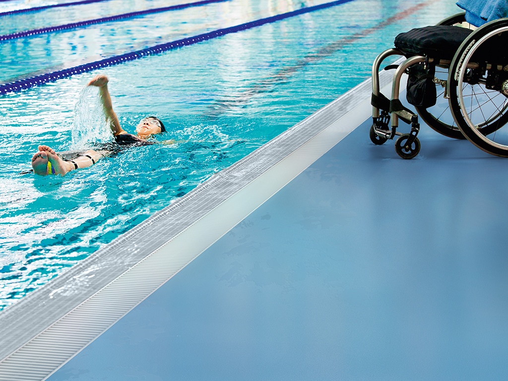 BYR8C8 a paraplegic woman swims in a pool with her wheelchair at the edge of the pool; edmonton, alberta, canada