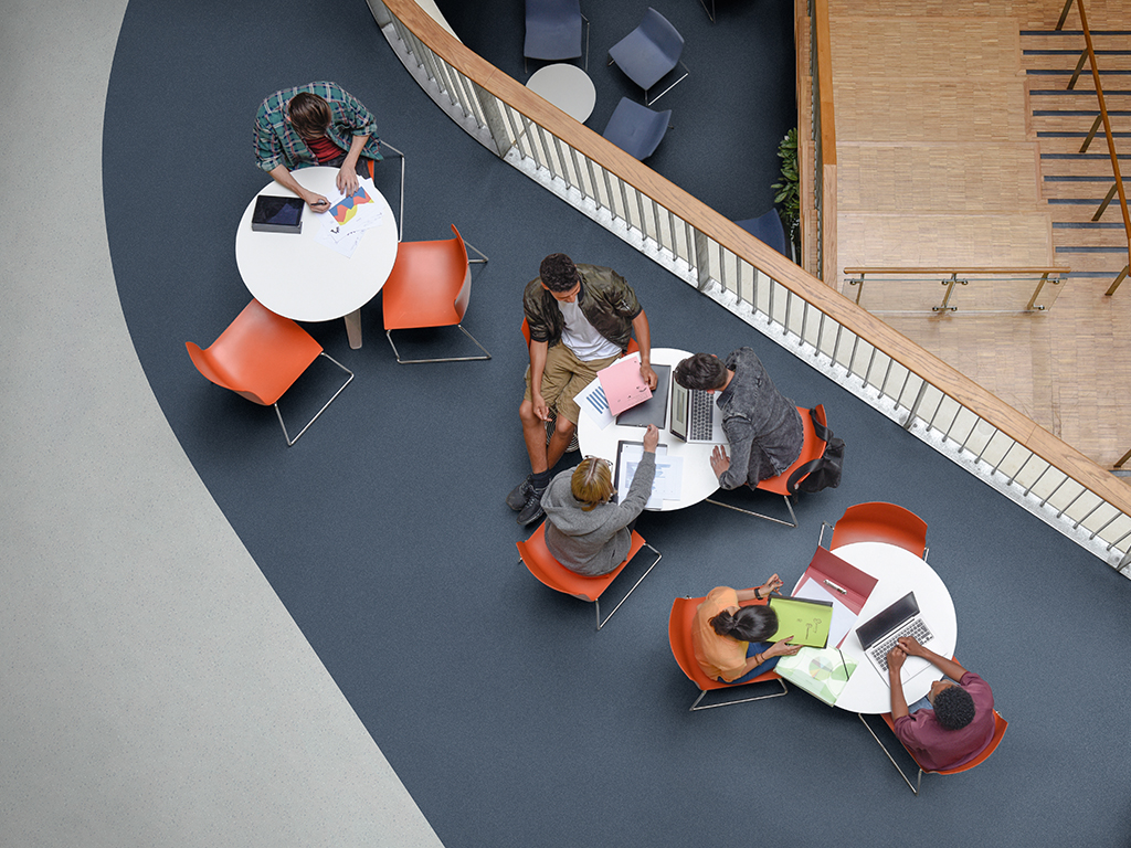 Young men and women studying in small groups around tables in FE college