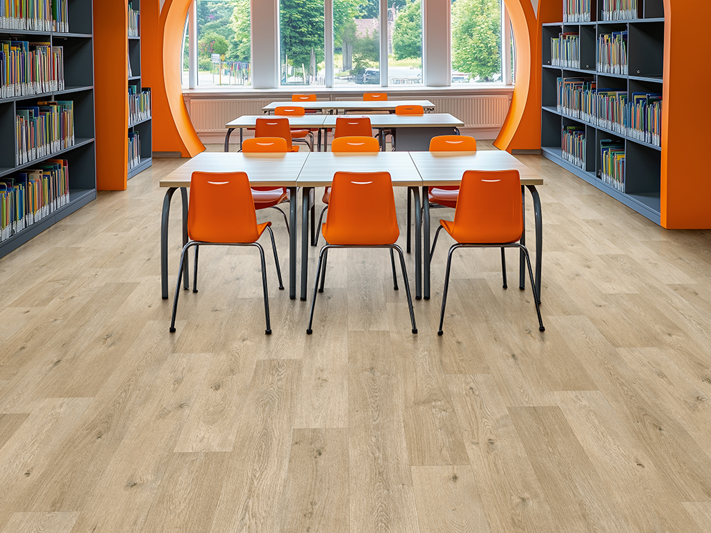 A school library featuring elegant modern archways, with ceiling-high shelves built into the arches. Charcoal grey desks and bright orange chairs with chrome legs bring vibrant contrast. The walls are